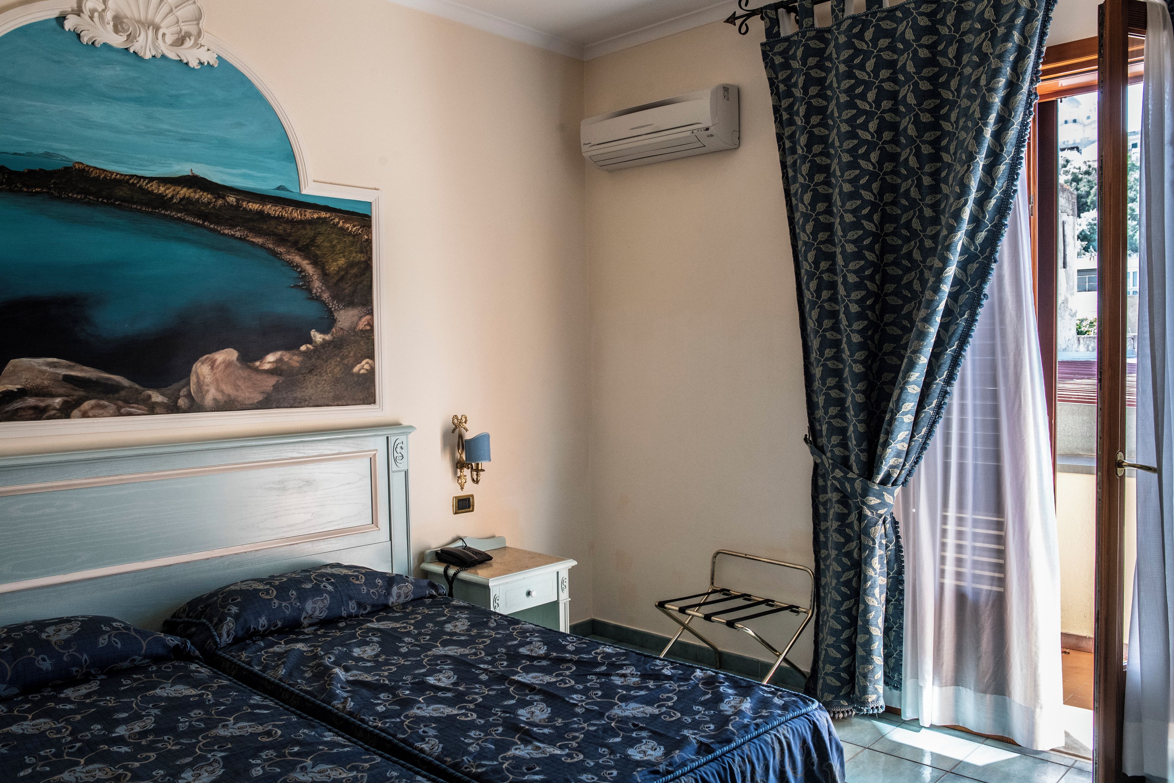A bedroom with a bed, a nightstand, a wall-mounted lamp, and a painting.