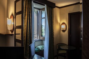 Habitación de hotel con ventana, un pequeño rincón de descanso con una silla y una mesa, y lámparas fijadas a la pared.