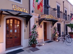 A hotel entrance with a large wooden door, a sign reading 'Hotel', and potted plants with flowers. - Hotel Garibaldi (Milazzo)