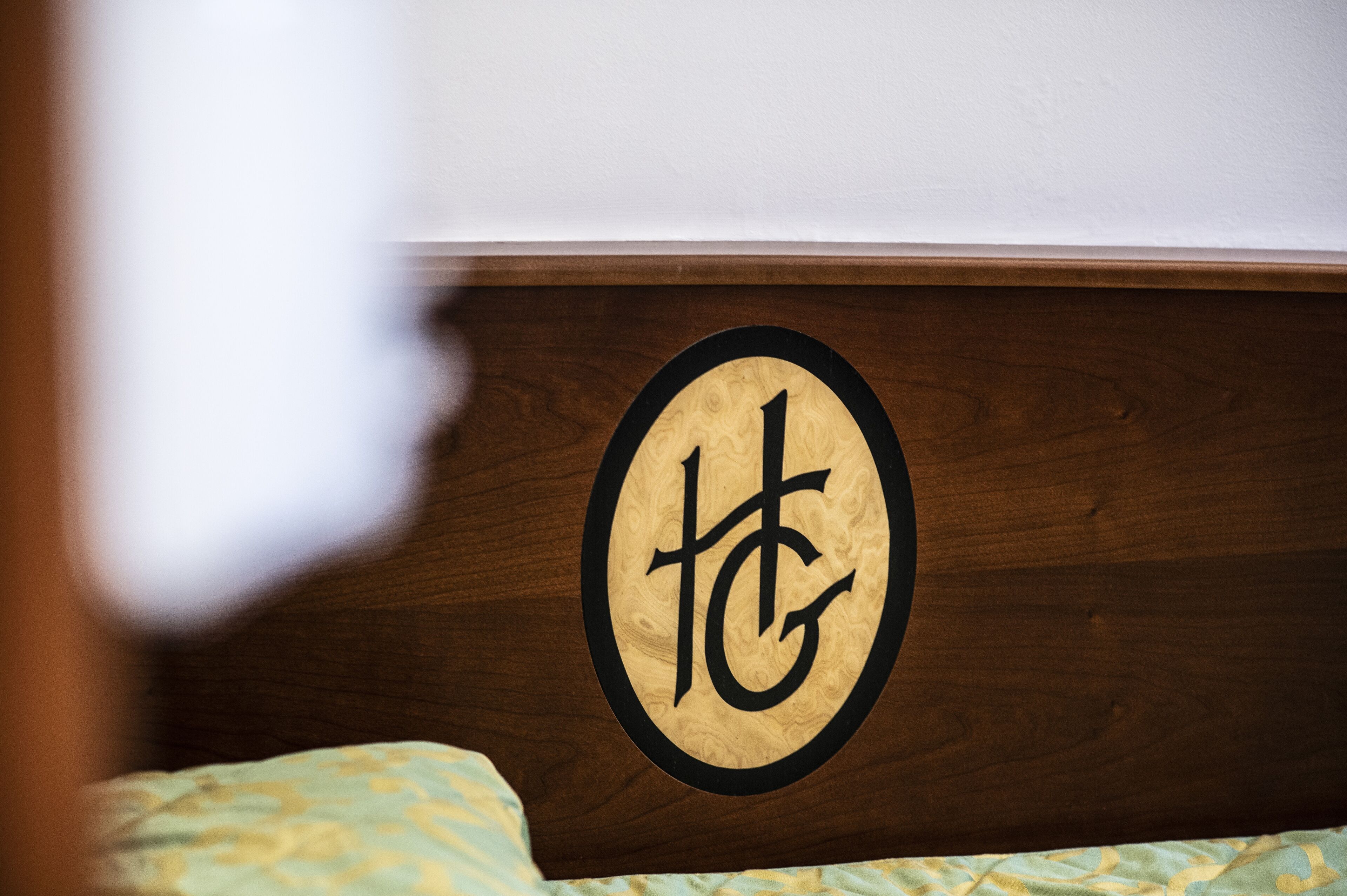 Une tête de lit en bois ornée d’un emblème circulaire représentant un logo stylisé « TG ».