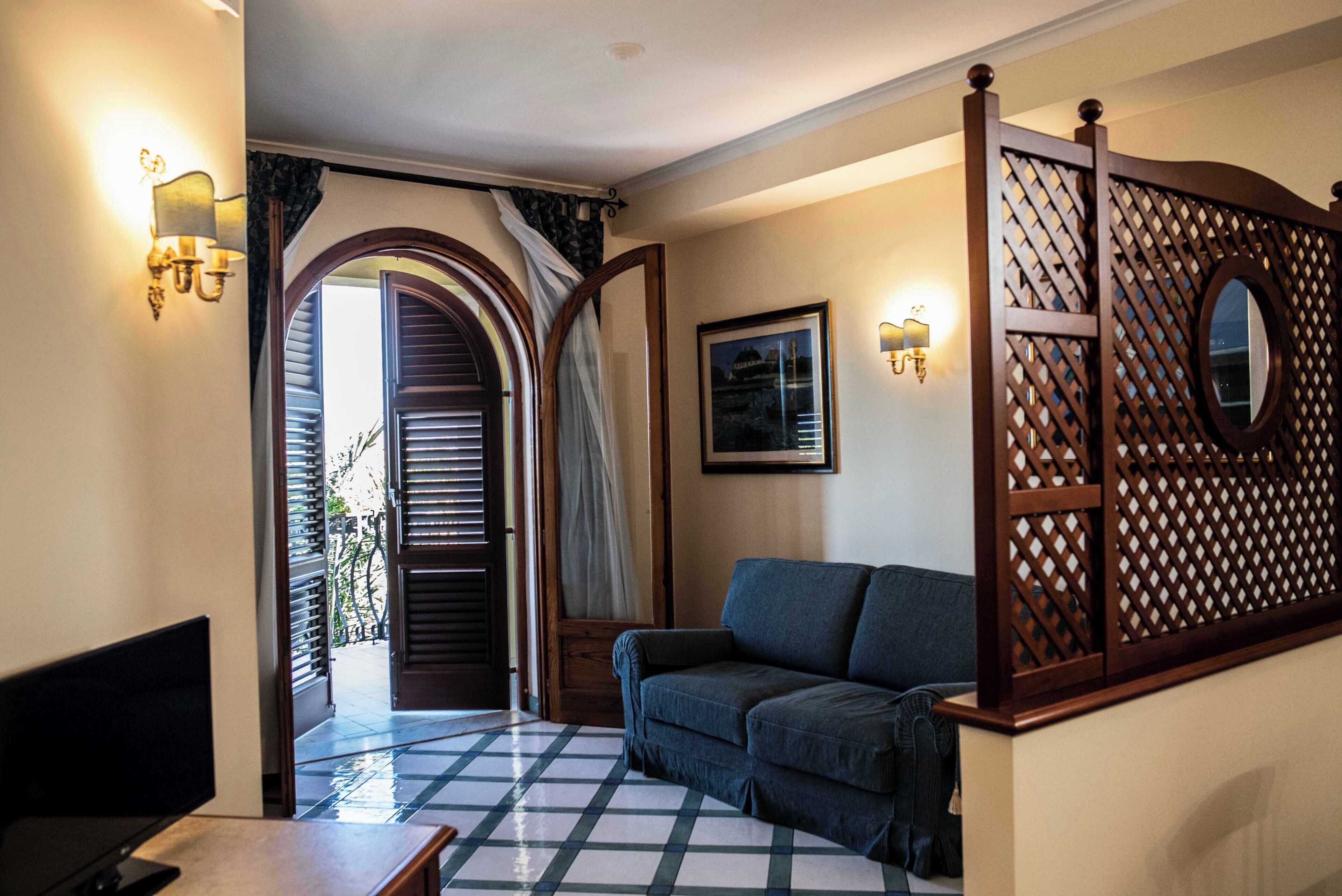 Habitación de hotel con piso a cuadros, un sofá, un televisor y un panel de madera con espejo.