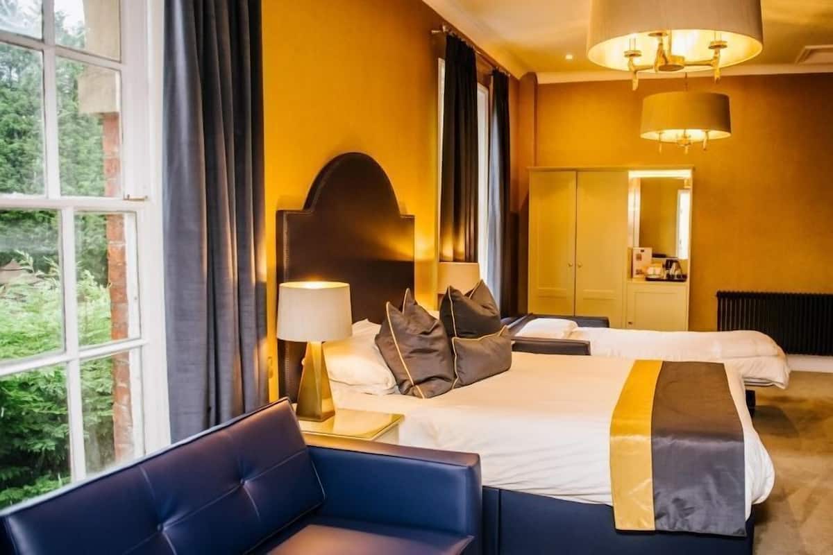 Quarto de hotel com duas camas, um sofá, um espelho e vista para áreas verdes.