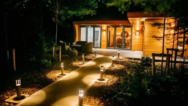 A modern building with a glass entrance, wooden exterior, and a pathway leading to a seating area.