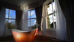 A spacious room with a large window, a modern bathtub, and a chandelier.
