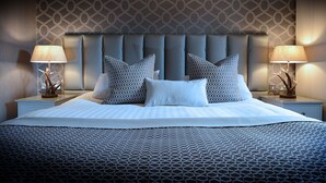 A large bed with a patterned bedspread, two matching pillows, and a headboard with a geometric design. There are two bedside tables with lamps and decorative items.