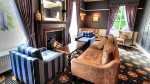 A room with a fireplace, striped armchairs, a brown sofa, and patterned carpet.