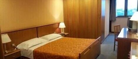 Una habitación de hotel con cama, escritorio, silla, televisor y ventana.