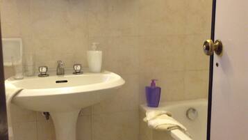 A bathroom with a pedestal sink, a mirror, a bathtub, and a door.