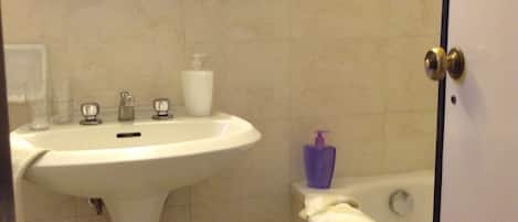 Ein Badezimmer mit einem Standwaschbecken, einem Spiegel, einer Badewanne und einer Tür.