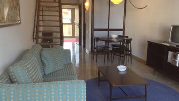 A living room with a sofa, a table, and a television. There is a staircase leading to another room.