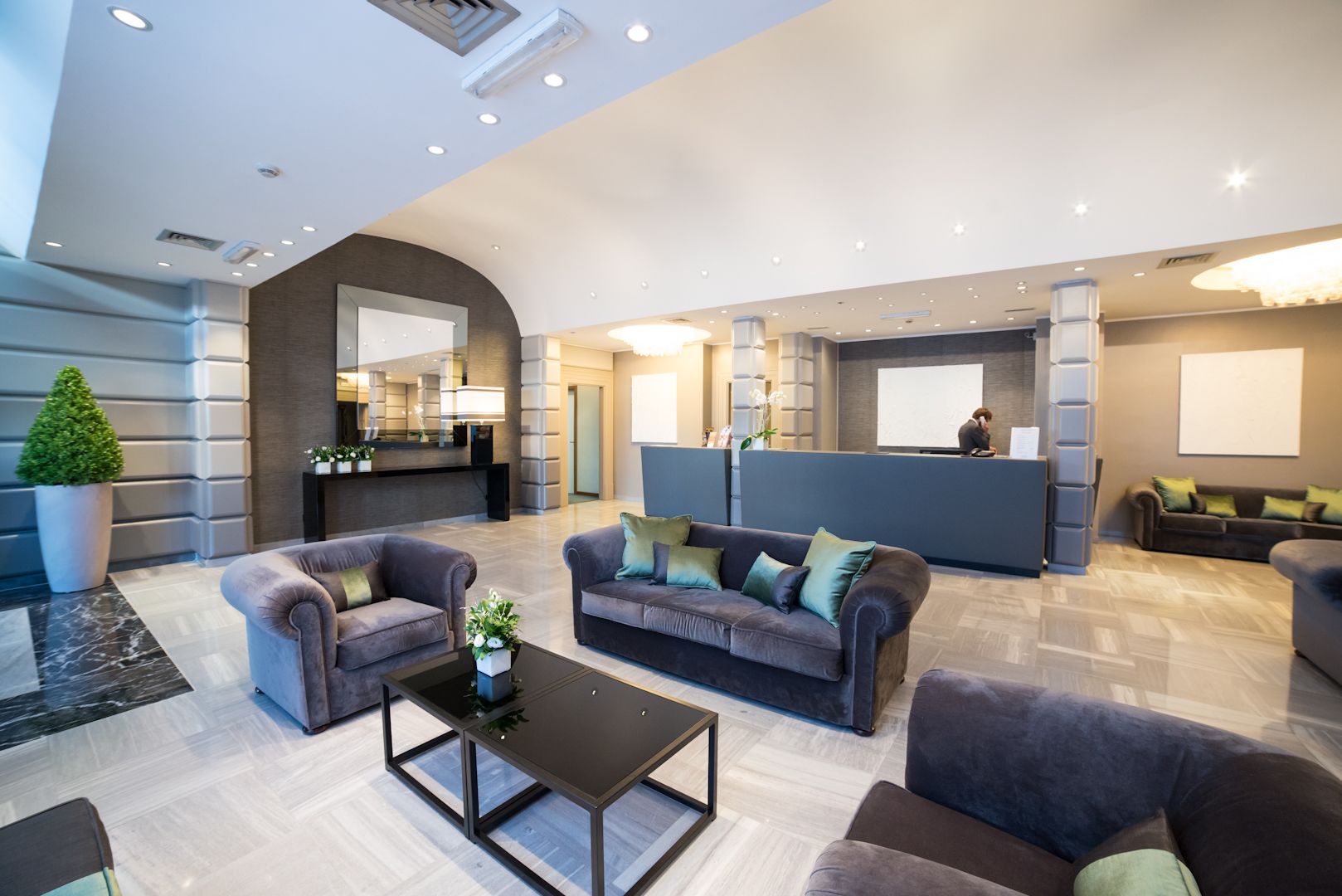 A modern lobby with sofas, a reception desk, and a large potted plant.