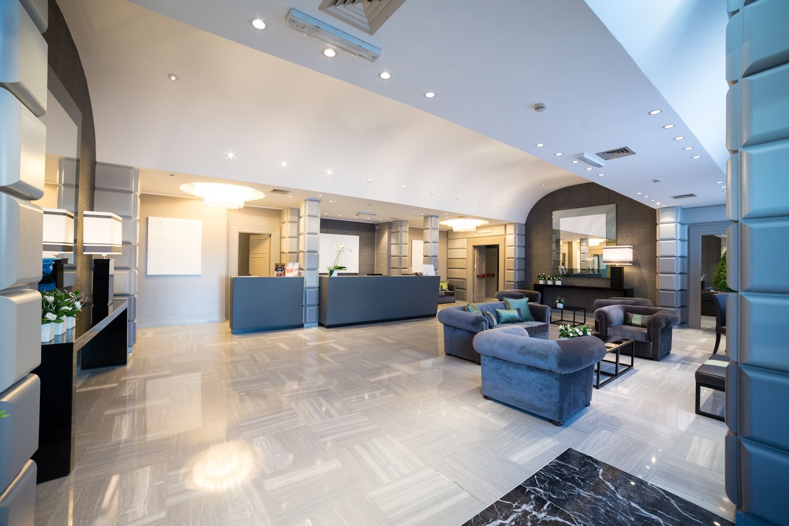 A spacious lobby with a reception desk, seating area, and a large mirror reflecting the space.