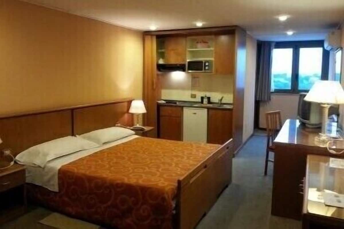 Ein kompaktes Hotelzimmer mit Bett, Schreibtisch, Stuhl, Mikrowelle und einer kleinen Küchenzeile.