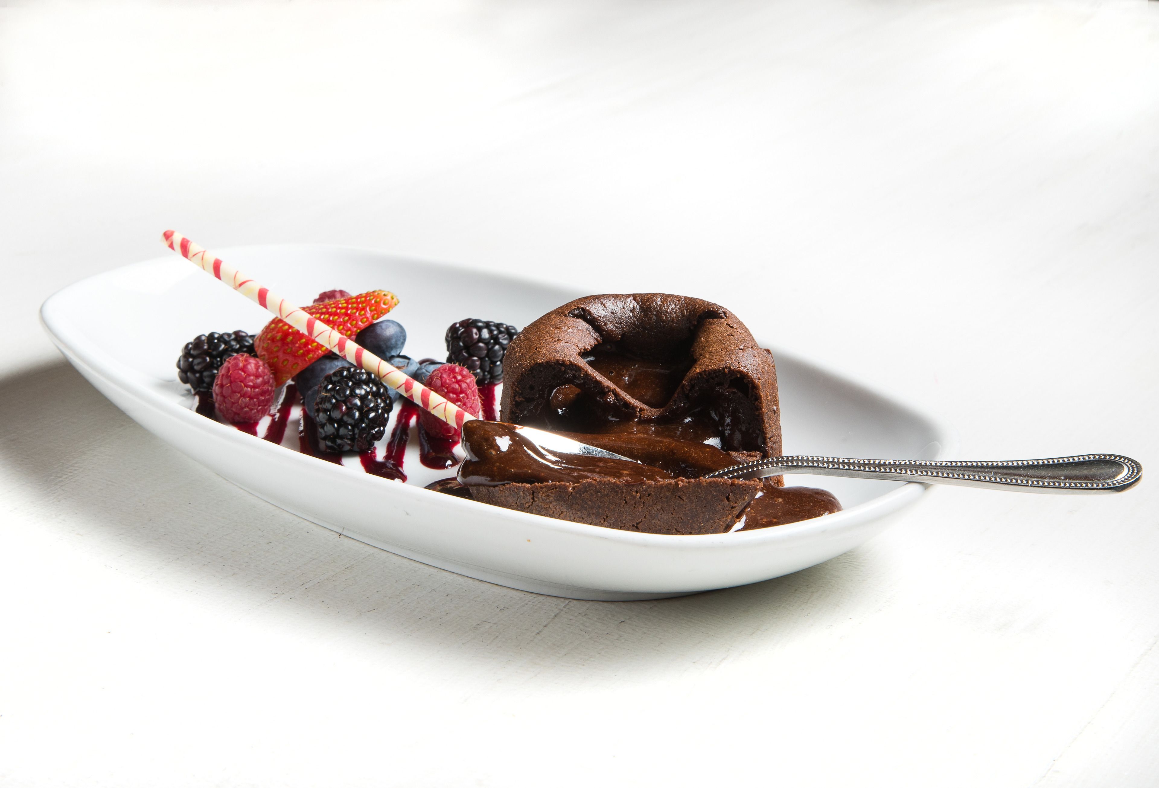 A chocolate lava cake with berries and a striped straw on a white plate.
