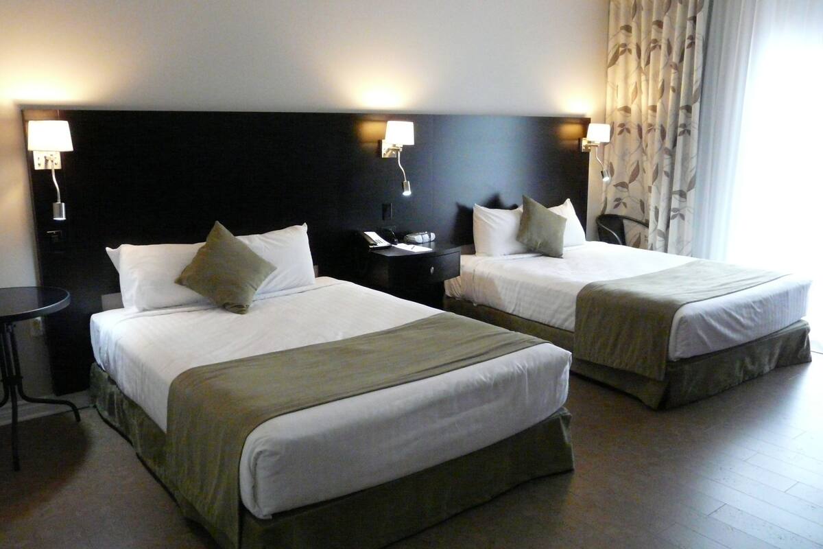A hotel room with two beds, each with a headboard, bedside tables, and lamps.