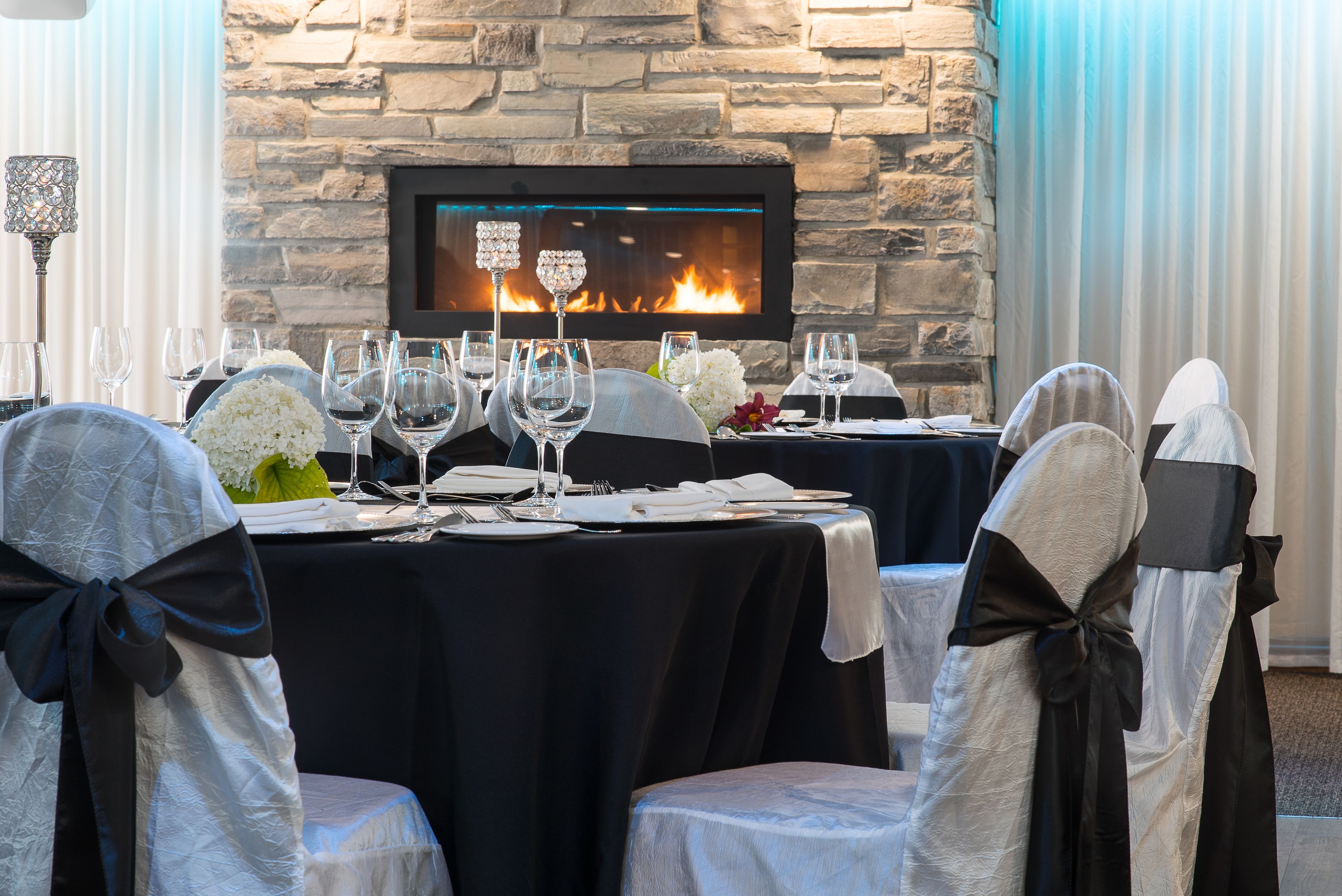 A dining area with a stone fireplace, black tablecloths, and chairs with black sashes.