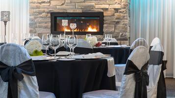 A dining area with a stone fireplace, black tablecloths, and chairs with black sashes.