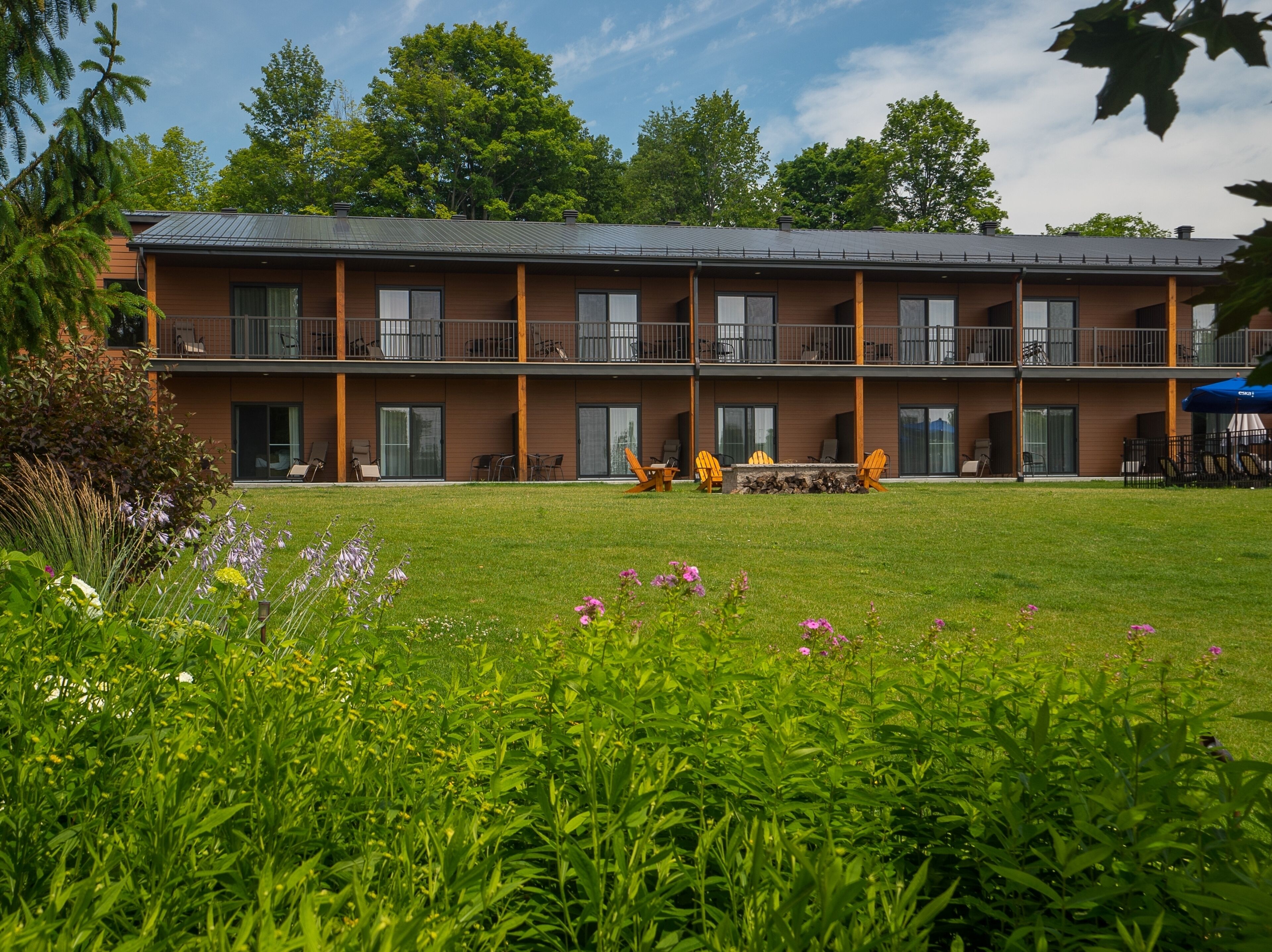 Ein zweistöckiges Motel mit flachem Dach, großen Fenstern und einer überdachten Außenbereich mit Stühlen und Tischen.