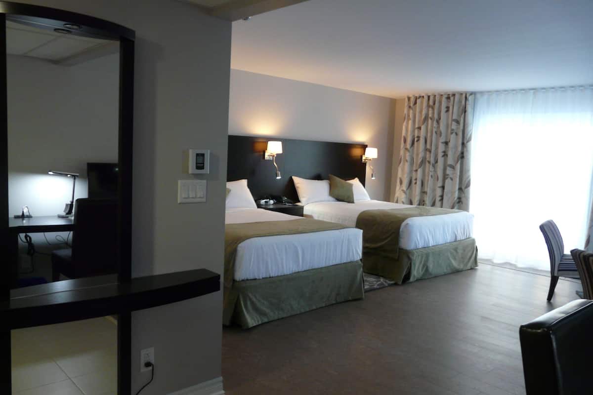 A hotel room with two beds, a desk with a chair, a mirror, and a window with curtains.