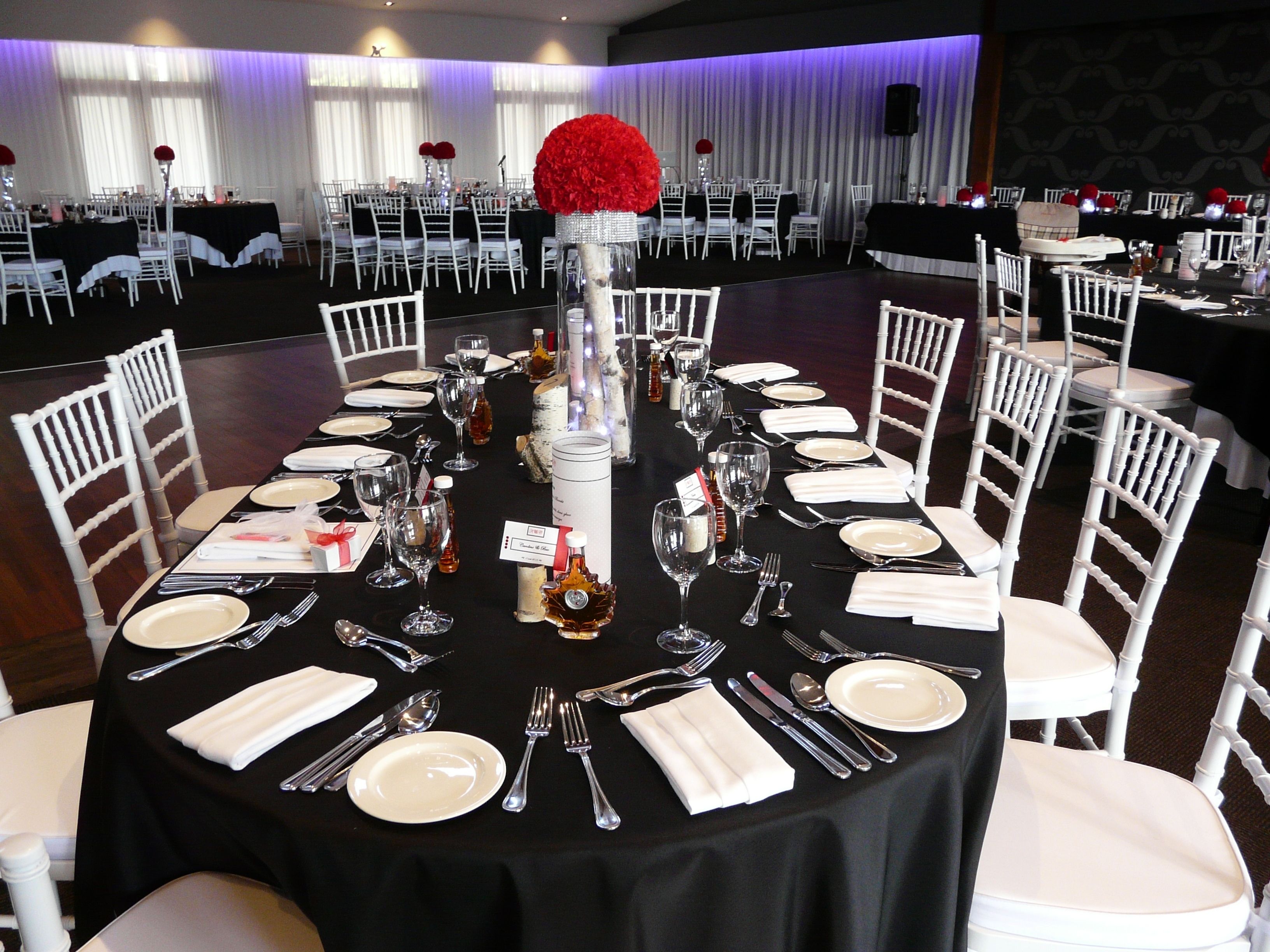 A banquet hall with round tables set for a formal event, featuring white chairs and black tablecloths.