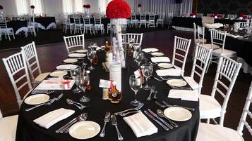 Un salón de banquetes con mesas redondas dispuestas para un evento formal, con sillas blancas y manteles negros.
