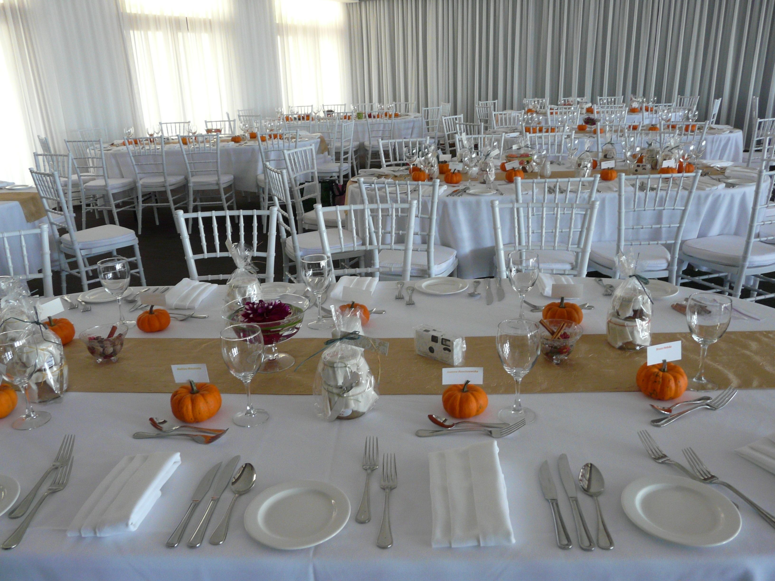 A banquet hall with multiple round tables set for a formal event, each with white tablecloths, silverware, and glassware.