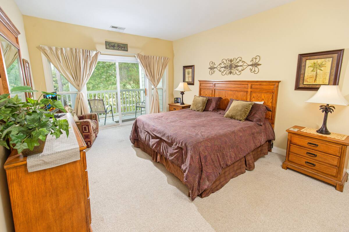 A bedroom with a large bed, wooden nightstands, a dresser, and a balcony with curtains.