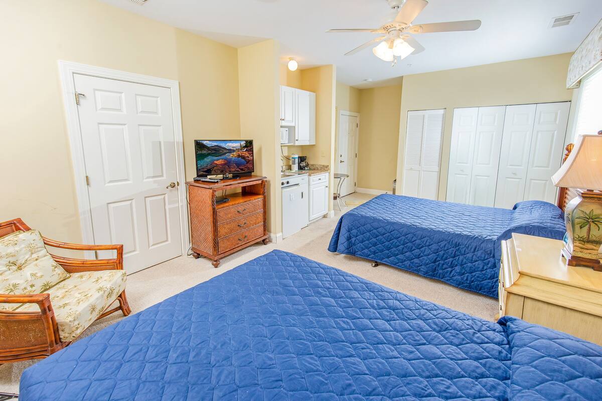 A hotel room with two beds, a television, a dresser, a chair, and a ceiling fan.
