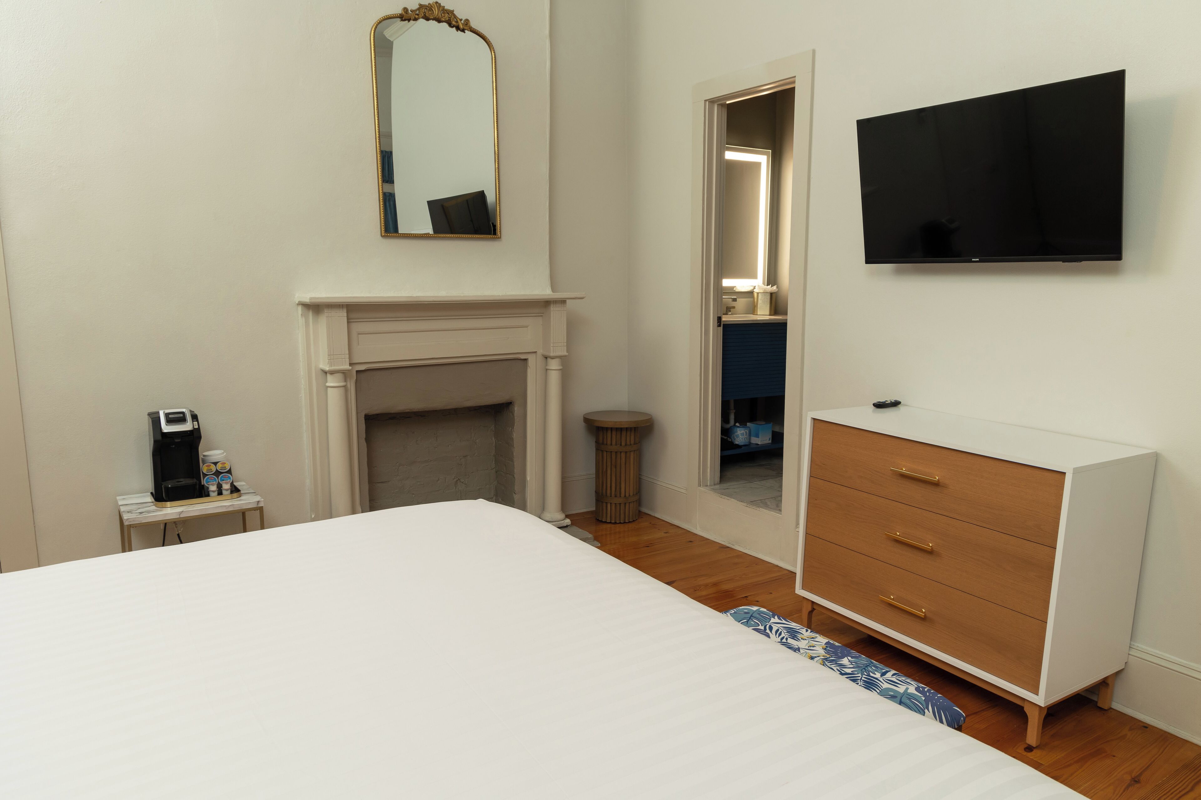 Une chambre à coucher comprenant un lit, une commode, un téléviseur, un miroir et une cheminée.