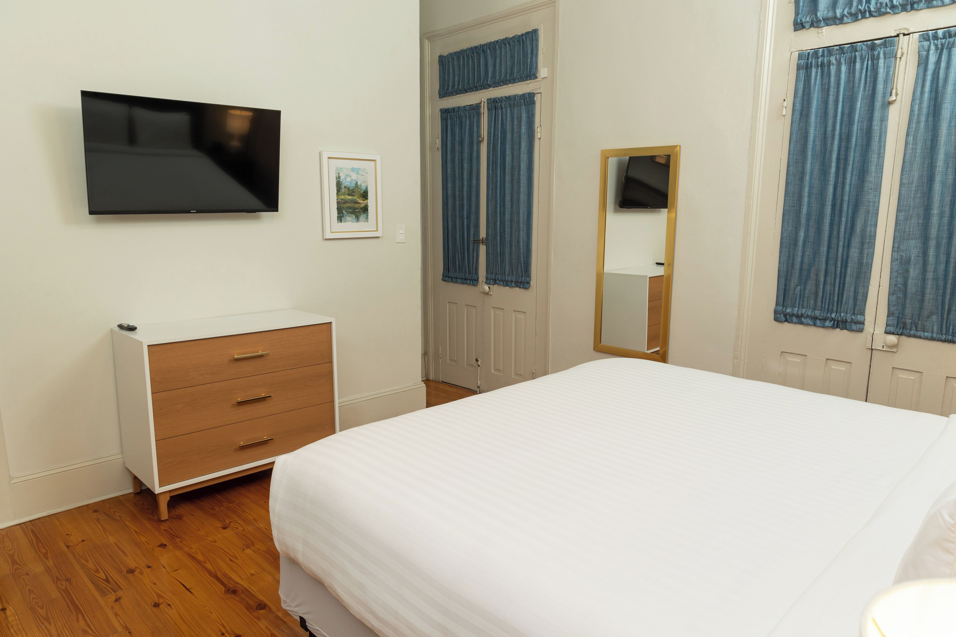A bedroom with a bed, a dresser, a television mounted on the wall, and a door with curtains.