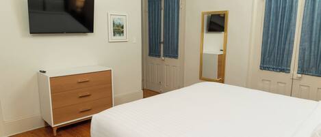 A bedroom with a bed, a dresser, a television mounted on the wall, and a door with curtains.