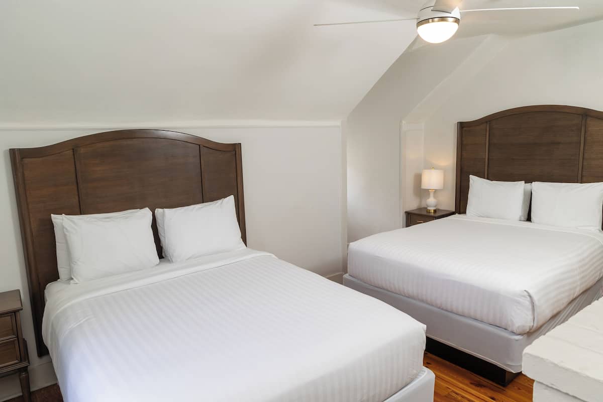 Duas camas de solteiro com cabeceiras de madeira num quarto com paredes brancas e teto inclinado.