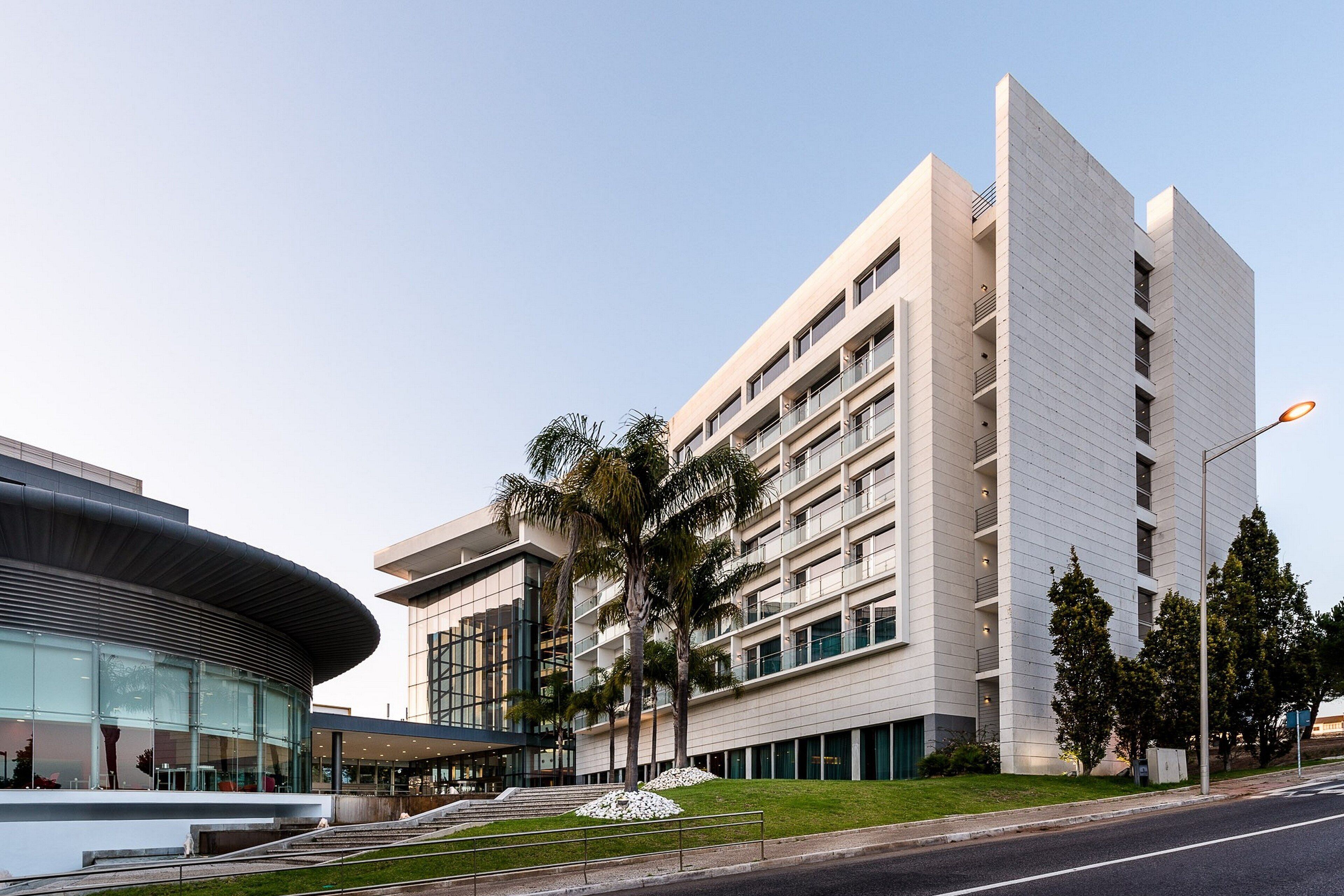 Un edificio moderno con fachada de vidrio curva, varios balcones y un césped bien cuidado.