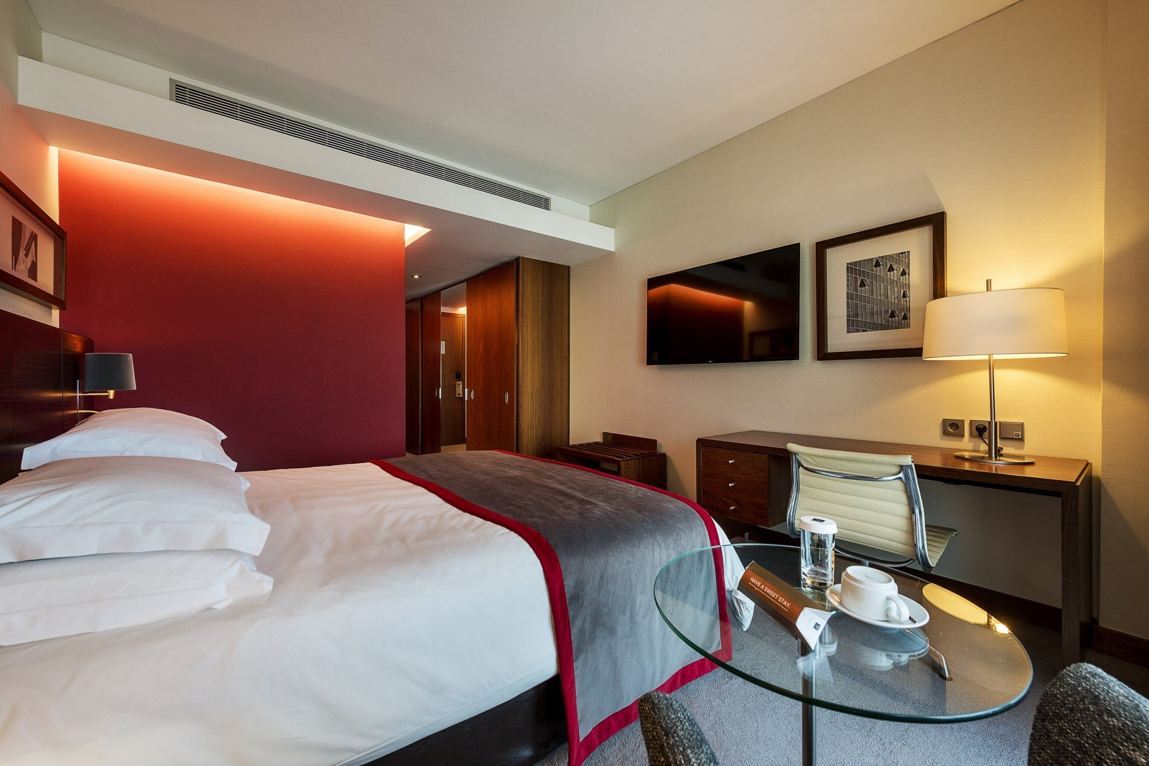 Une chambre d’hôtel avec un lit, un bureau, une chaise, une table et un téléviseur.