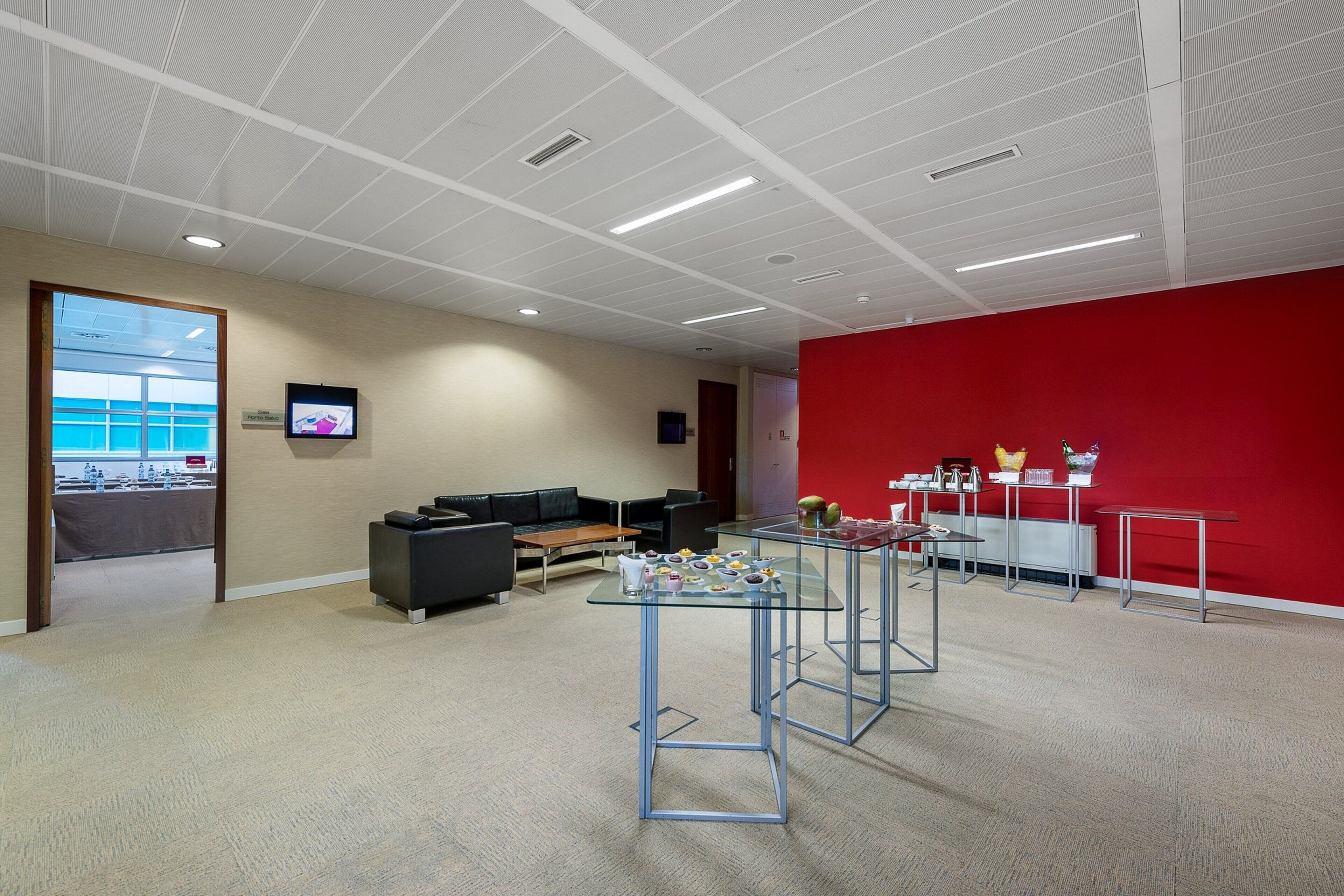 A modern office space with a red accent wall, a reception area with a counter, and a seating area with a couch and tables.