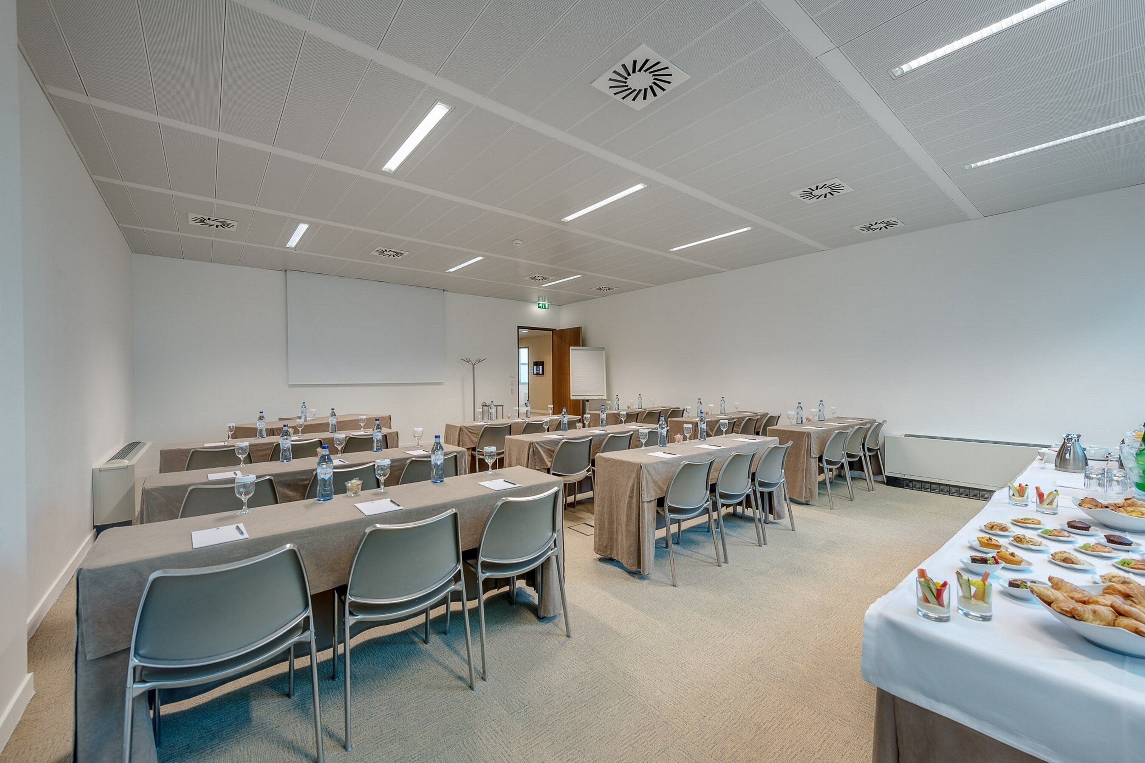 A conference room with multiple tables, chairs, and a buffet table with food and drinks.