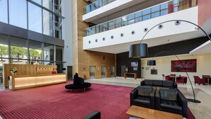 En rummelig lobby med rød løber, sorte lædersofaer, en træreception og et moderne loftdesign.