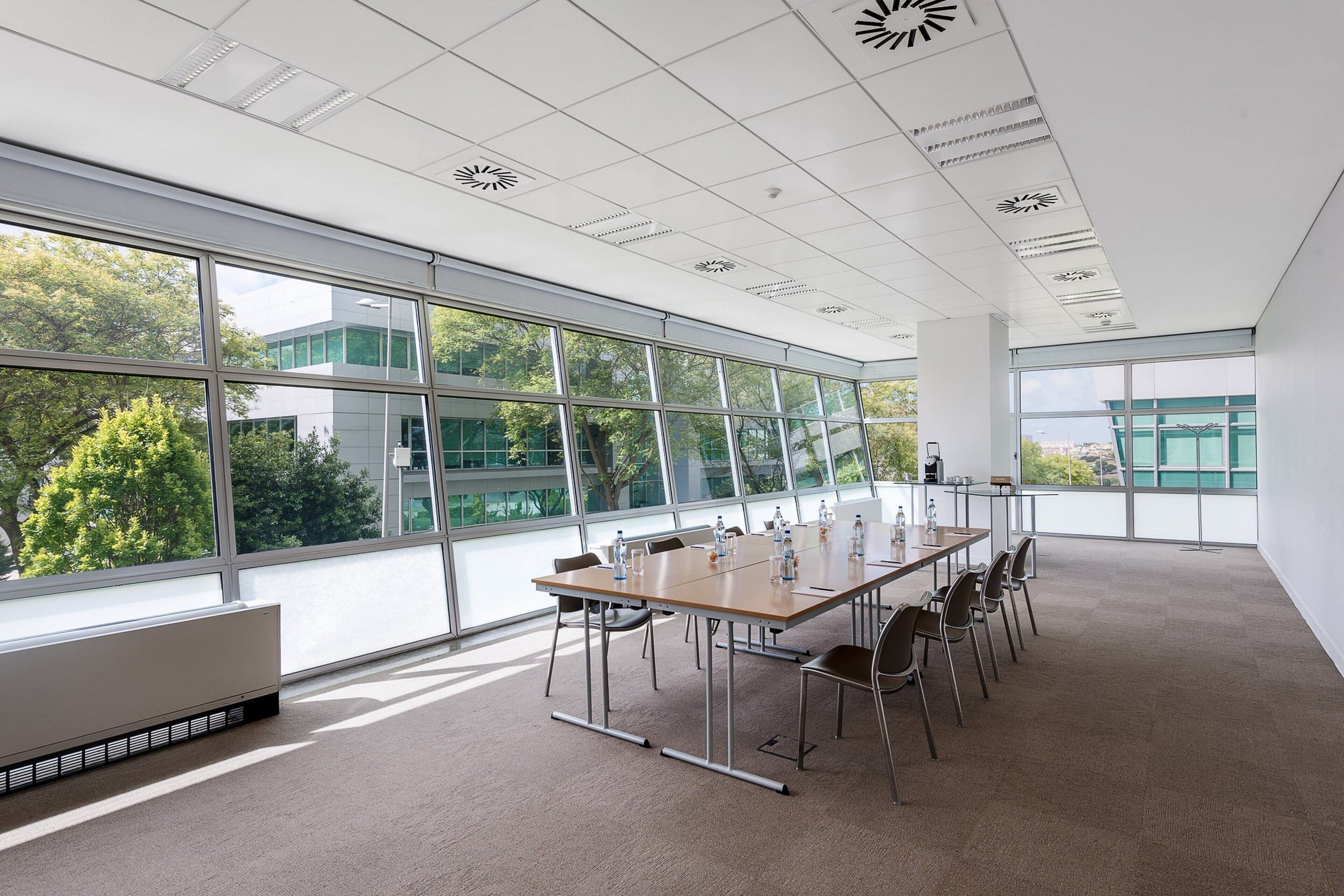 Un salón de conferencias con una gran mesa, sillas y vistas a árboles y edificios a través de amplias ventanas.