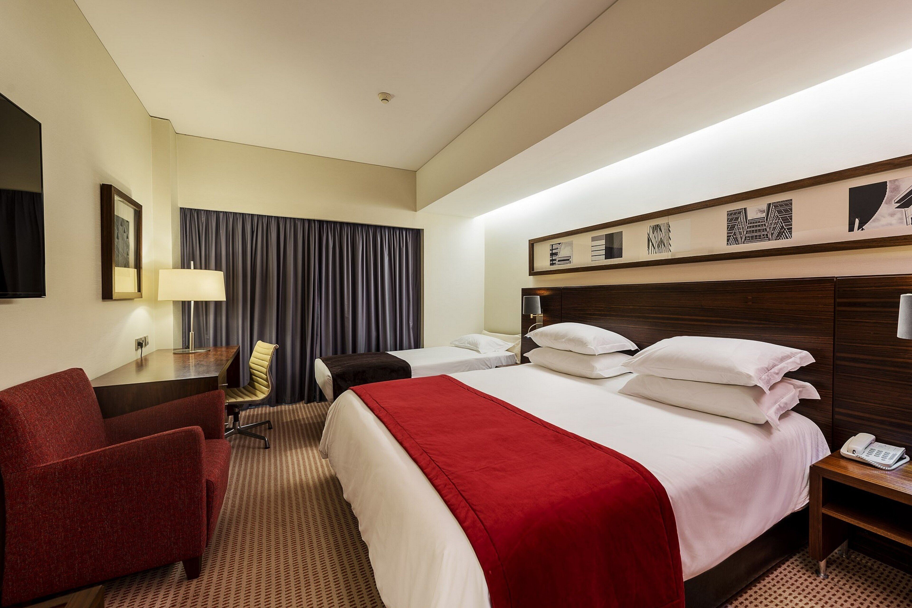 Una habitación de hotel con una cama grande, un escritorio, una silla, una lámpara y un teléfono.