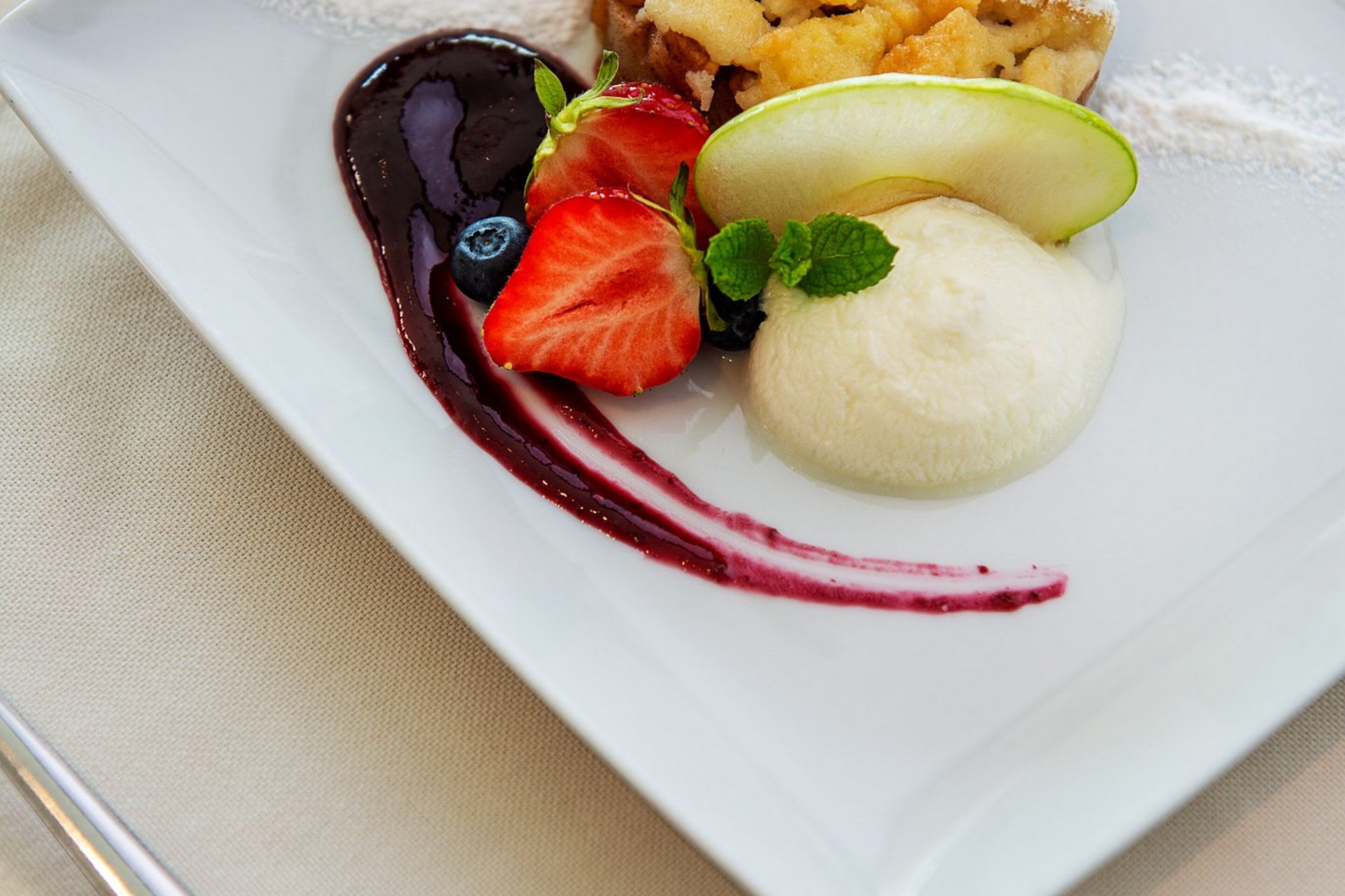 Un plato de postre con helado, fruta y salsa de frutos rojos.