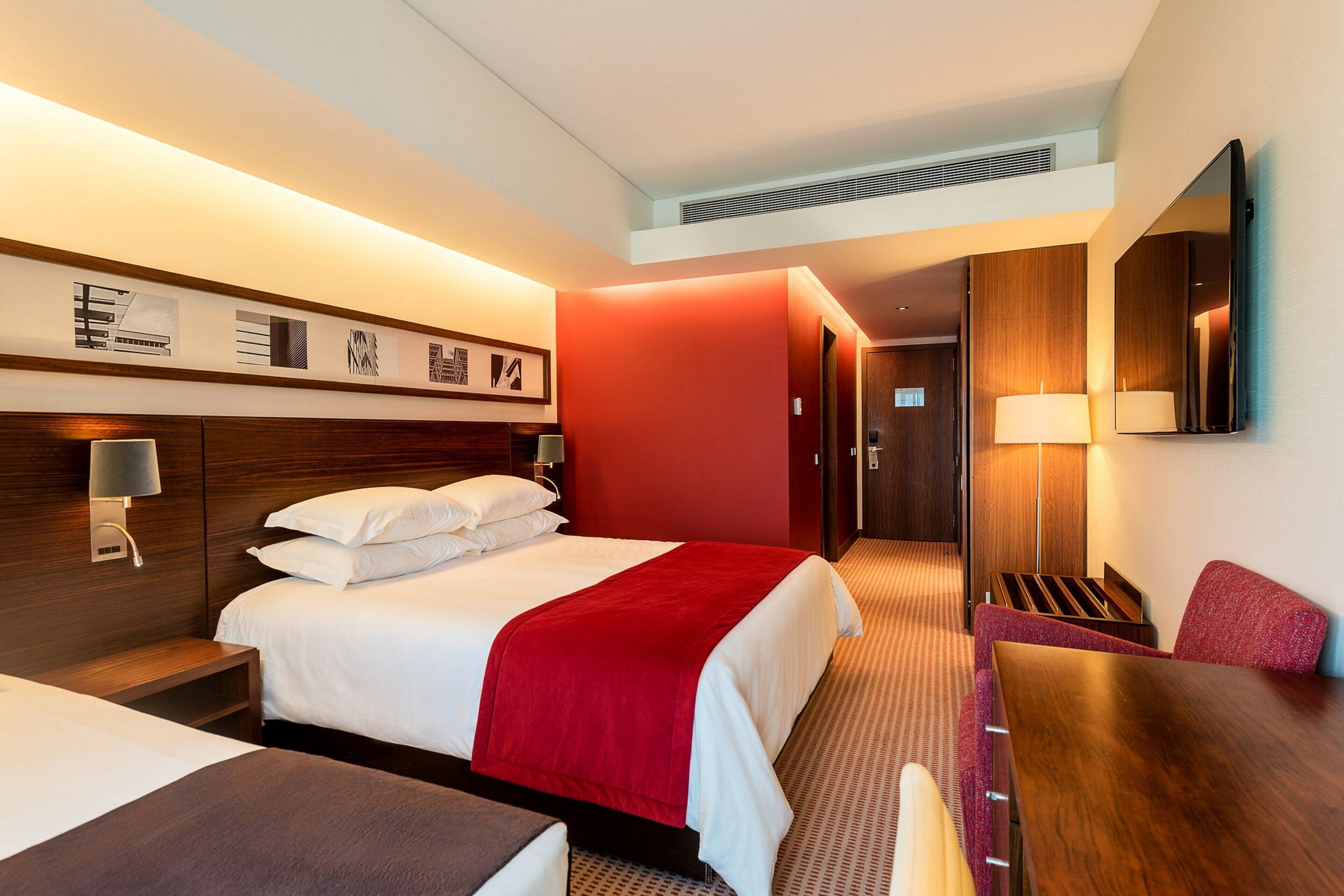 Une chambre d’hôtel comprenant un lit, une table de chevet, une lampe et un bureau avec une chaise.