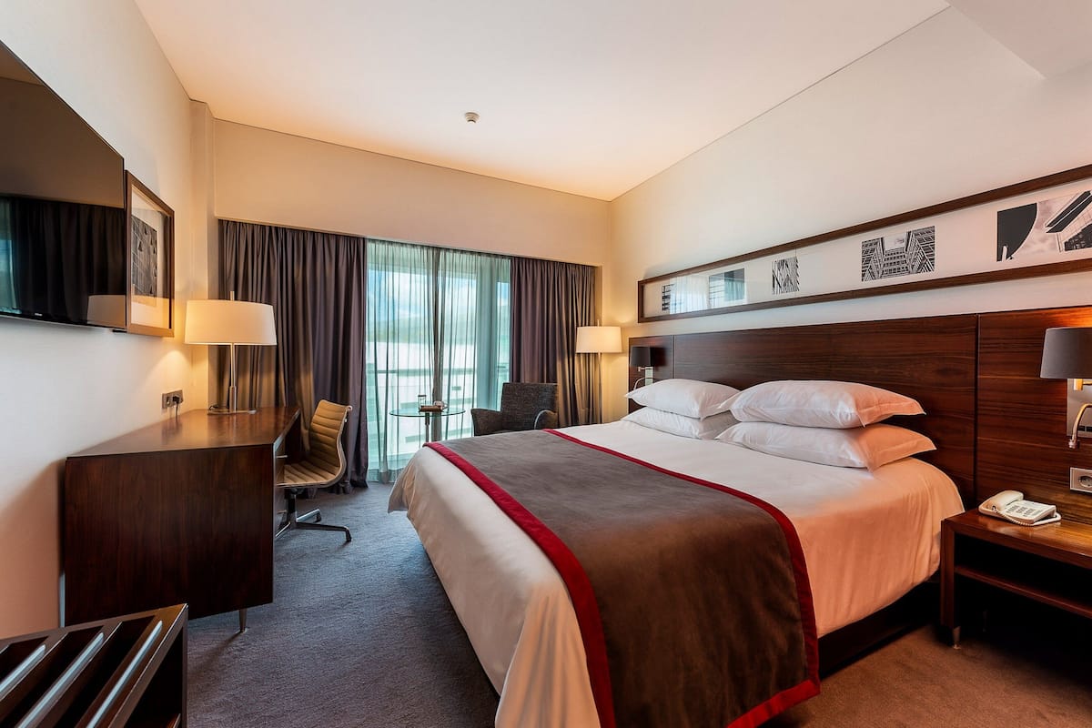 Ein Hotelzimmer mit einem großen Bett, einem Schreibtisch, einem Sessel, einem Fernseher und einem Telefon.
