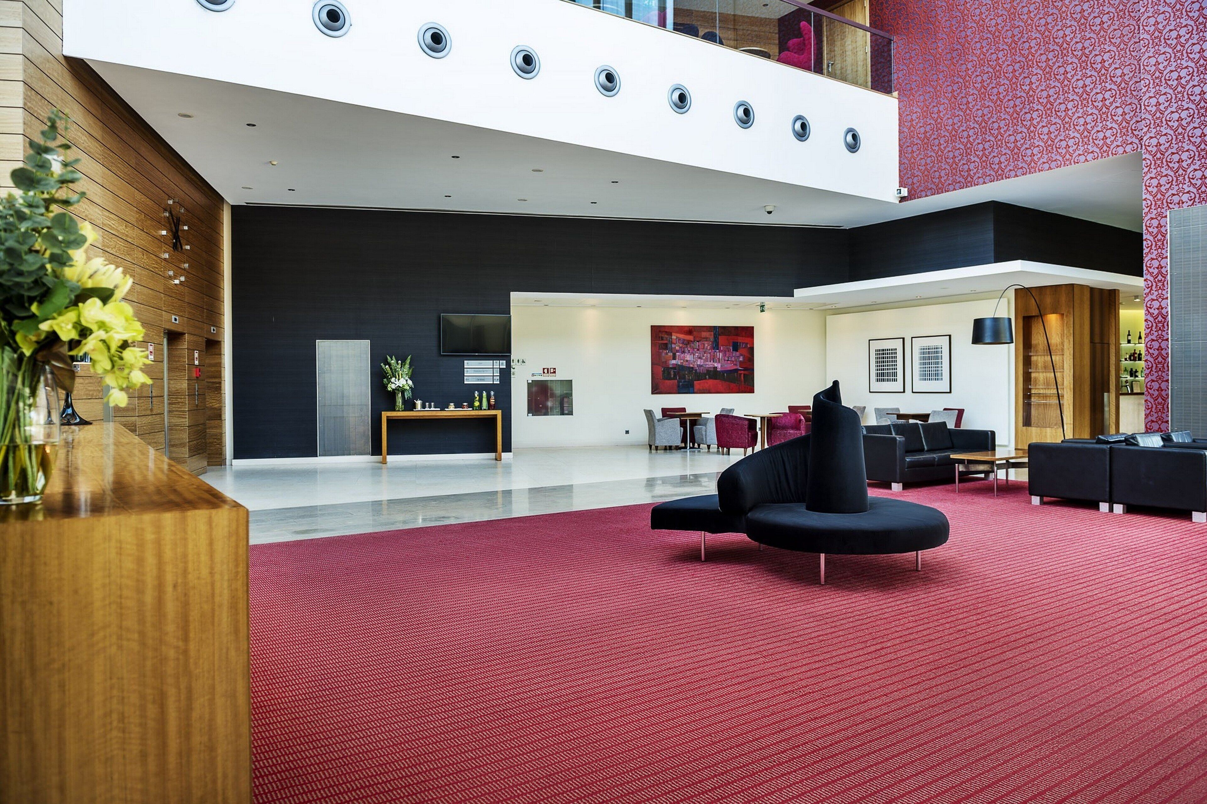 Un hall d’entrée moderne avec un tapis rouge, des canapés noirs et un comptoir d’accueil en bois.