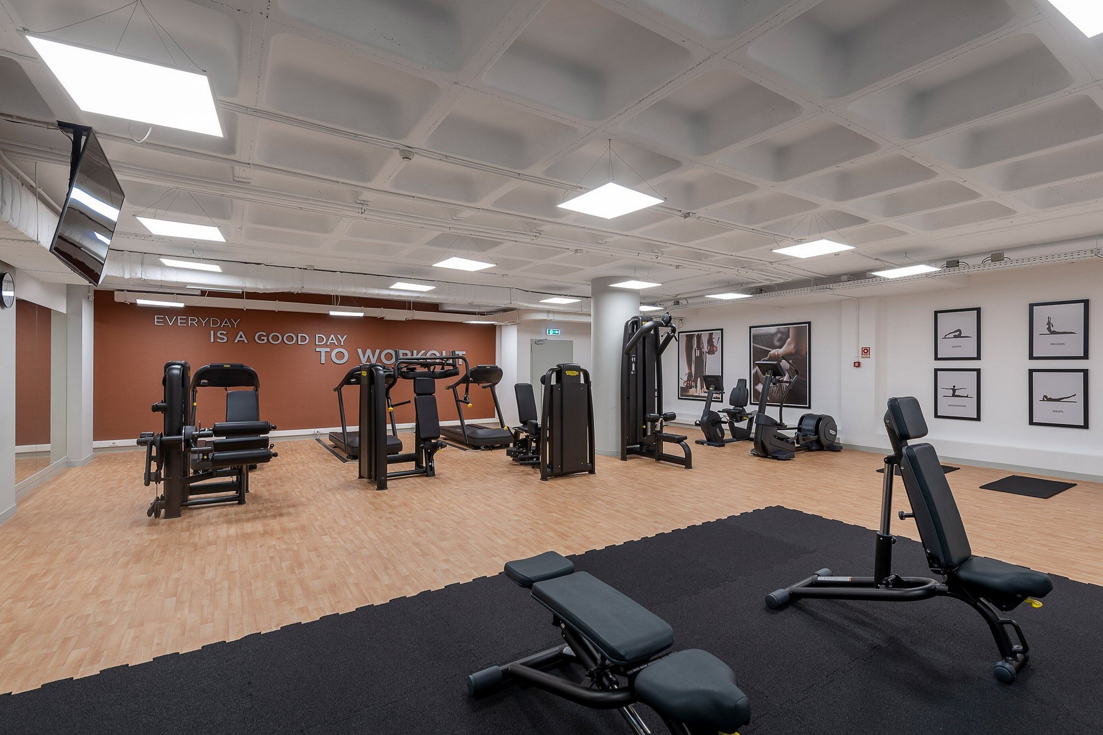 A gym with various exercise equipment, a motivational wall, and a black mat area.
