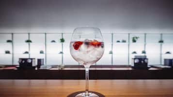 A glass of iced beverage with fruit on a wooden table in a room with a white wall and shelves in the background.