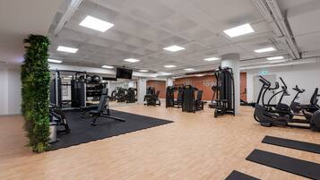Un gimnasio con diverso equipo de ejercicio, un espejo grande y una pared con frases motivacionales.