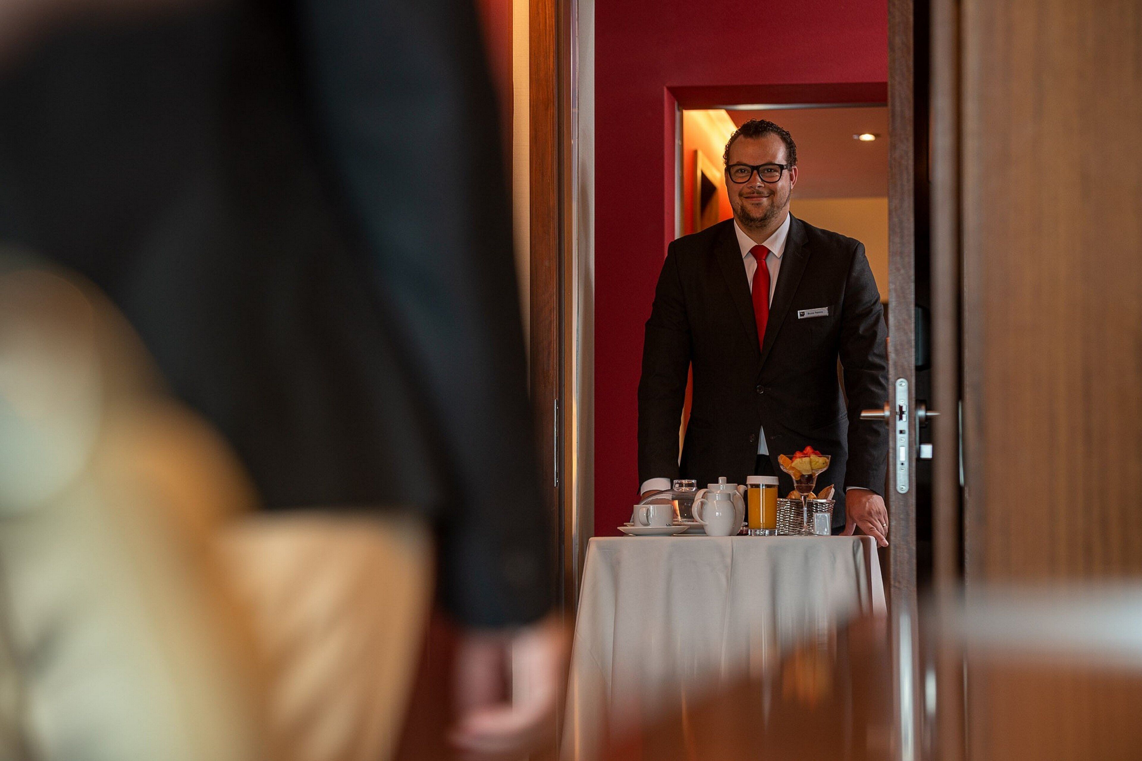 Une chambre d’hôtel avec une table mise pour le petit-déjeuner, comprenant une théière, des tasses et un panier de fruits.