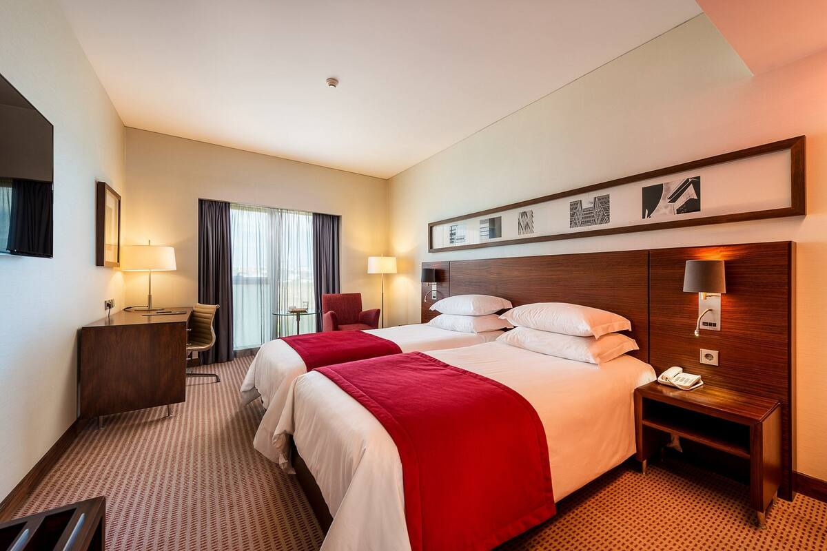 Ein Hotelzimmer mit zwei Betten, einem Schreibtisch, einem Stuhl, einem Fernseher und Bildern an der Wand.