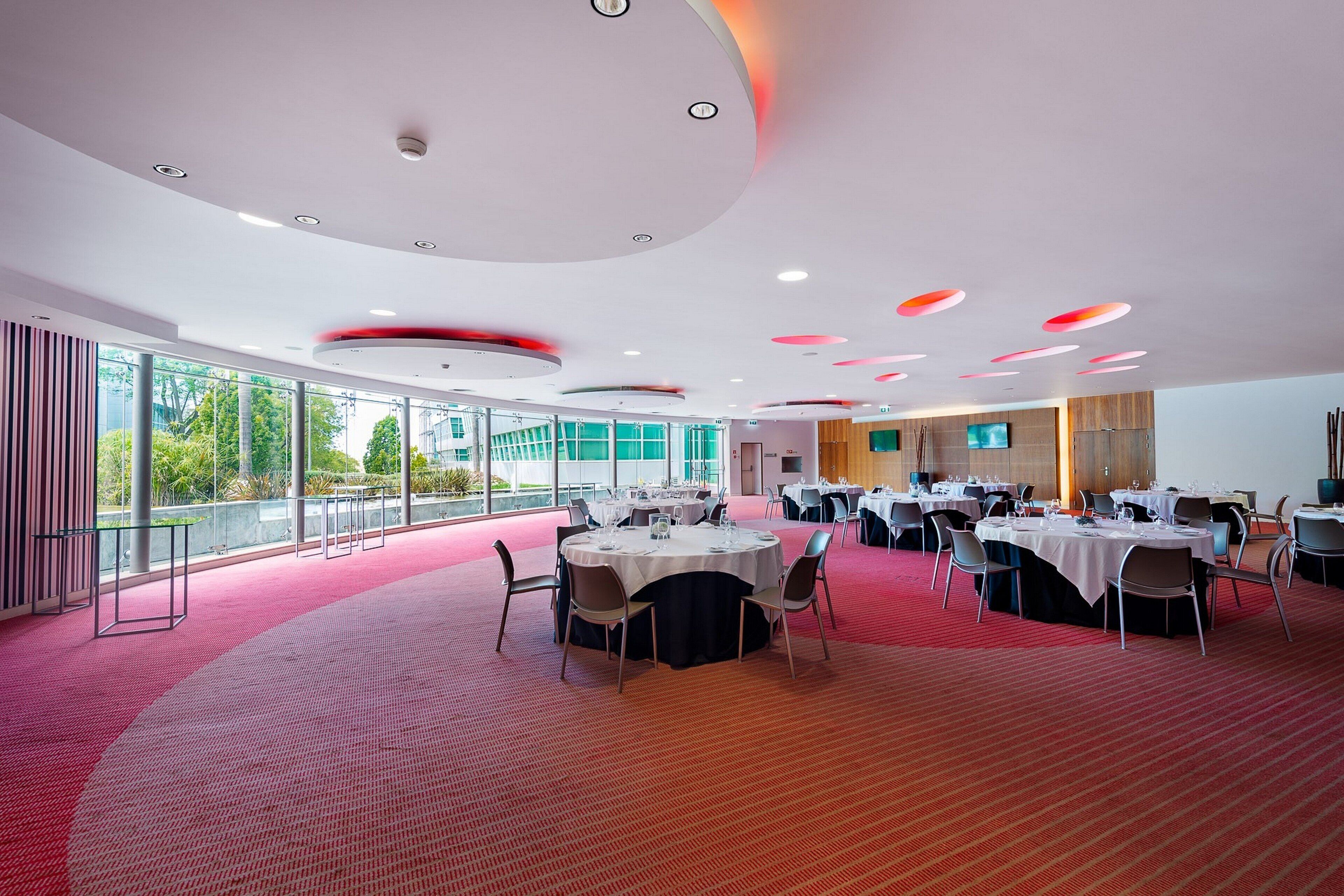 Una sala de conferències espaiosa amb taules rodones, grans finestres i un disseny de sostre modern.
