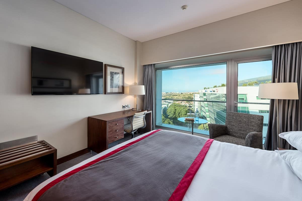 Ein Hotelzimmer mit einem großen Bett, einem Schreibtisch, einem Stuhl, einem Fernseher und einem Balkon mit Blick.
